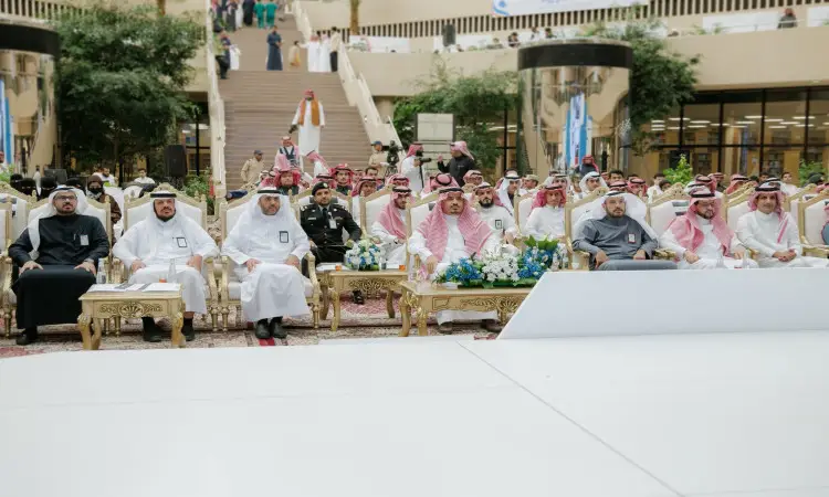 At home at Qassim University, a large number of men wearing the Saudi ghattra or shemagh and aqal, as well as the Saudi bisht, sit on an outdoor patio. Attendees and photographers sign autographs by the stairs and greenery, as part of the Nazaha Clubs event.