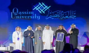 مجموعة من الرجال الذين يرتدون الغترة أو الشماغ مع العقال والبشتاء السعودي، اللمسون على منصة الحدث في مناسبة لكريم الجهود الرقمية، حيث أظهر أحدهم عصر شهادة تقديرية. ويبرز خلفهم شعار جامعة القصيم مكتوبًا باللغتين العربية والإنجليزية.