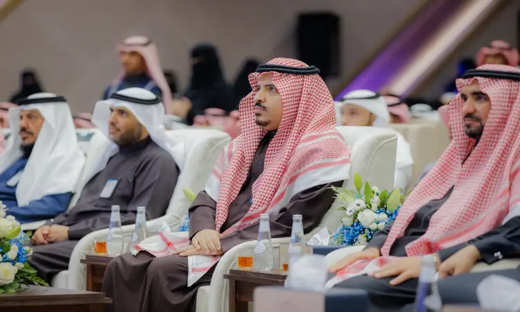 يجتمع مجموعة من الرجال الحاضرين الغترة أو الشماغ السعودي مع العقال والبشت السعودي، في فعالية جامعية في القصيم احتفاءً بـإنجازات الطلاب. يحضر باهتمام حول طاولات تزينها باقات الزهور وقوارير المياه، بينما يظهر آخر عدد من المشاركين في يوم الطالب.