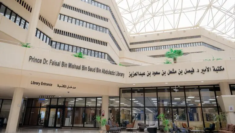 The entrance to a spacious library characterized by large doors and beige columns bearing signs in Arabic and English for "The Library of His Royal Highness Prince Dr. Faisal bin Meshal bin Saud bin Abdulaziz". This scientific edifice is supervised by the General Administration of Libraries, a knowledge resource center, illuminated by a glass window. The academic elites of the university students flock to this place, wearing the shemagh or the ghutra with their headband, accepting the official Saudi winter, and maintaining the dignity of the presence and its venerable character.
