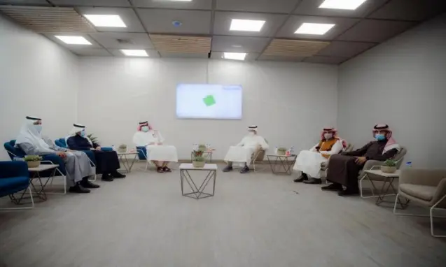 مجموعة ستة رجال يرتدون شماغ السعودي أو الغترة السعودية متباعدين في القاعة العصرية الحديثة ديكور الحد الأدنى، خلفهم شاشة كبيرة يتم عرضها تقريرًا عن الهدف السادس.