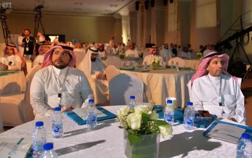 اعتصام مجموعة من الرجال مرتدين الشماغ أو الغترة السعودية وأزياء تقليدية في قاعة داخلية، حيث تتوزع عليها طاولات يجتمعون بالمياه والزهور وبعض الوثائق، وذلك من خلال حضورهم لفعاليات مؤتمر رسمي يُناقشتقريرًا متعلقًا بالهدف السادس. حيث يحضر بعض منصتين باهتمام للنقاشات المطروحة، بينما يتأمل أكرا أرجاء القاعة.