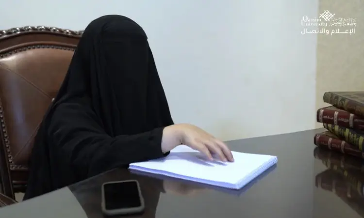 يرتدي نقابًا أسود يقرأ كتابًا مكتوبًا بطريقة برايل على مكتب، إلى جانبها هاتف ذكي وعد بكتب كبيرة مكدسة بالقرب منها. يظهر شعار جامعة القصيم وببارة "الهدف العاشر" في الجزء العلوي الأيمن من التقرير.