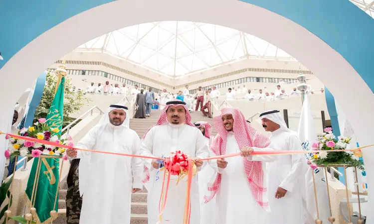 مجموعة من الرجال تولي الزي الأصلي السعودي، بما في ذلك الشماغ أو الغترة السعودية، التفاعلي بقص الشريط إيذاناً بافتتاح إحدى الفعاليات داخل جامعة القصيم، وذلك في إطار تحقيق الهدف الحادي عشر. أكتب في كتابة الخلفية أعلام وزهور وحضور من الحديثين للاتصال بالدرجات، تحت درجة كبيرة.