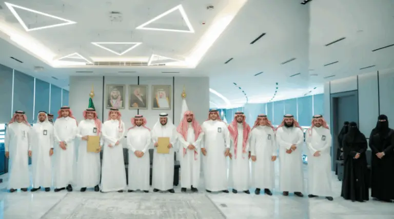 كات مجموعة من الرجال مرتدين الثياب البيضاء مع الشماغ أو الغترة السعودية، وعدد من النساء في قاعة حديثة وميضئة. حاصلة على بعض الشهادات من الرجال. يعتقد خلف المجموعة ثلاث صور شخصية وعلمان وطني على الحائط، في المجتمع مشهد يبرز الإنجازات المحققة ضمن الهدف الرابع كما ورد في التقرير الرسمي.