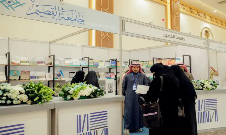 مجموعة من الزوار، من بينهم سيدات حضرن أذنات بيضاء اللون بزي سعودي تقليدي تشمل الشماغ أو الغترة السعودية، يتصفحون الكتب في جناح مضاءة بشكل مشرق ومزين بالزهور ضمن فعاليات معرض الكتاب. تحافظ على لوحات الصين لكتب الصين باللغة العربية وتتلخص في «الهدف الرابع».