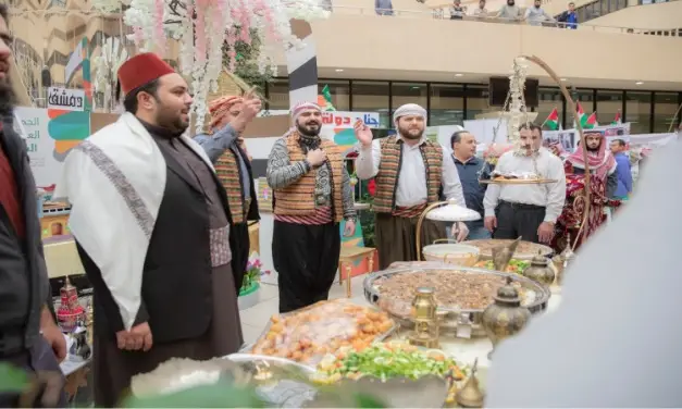 الاتصال مجموعة من الرجال مرتدين الزي التقليدي السعودي، بما في ذلك الشماغ أو الغترة السعودية، حول طاولة تحوي عدداً من الخيارات المتنوعة، وذلك ضمن فعالية تقام في إطار مهرجان ثقافي أو تجاري. وأشار بعض المشاركين وهم يتبادلون النقاش حول تقرير الهدف الرابع، في حين يقوم بتبادل التحلية والترحيب أو تطبيق مساهمات المأكولات.