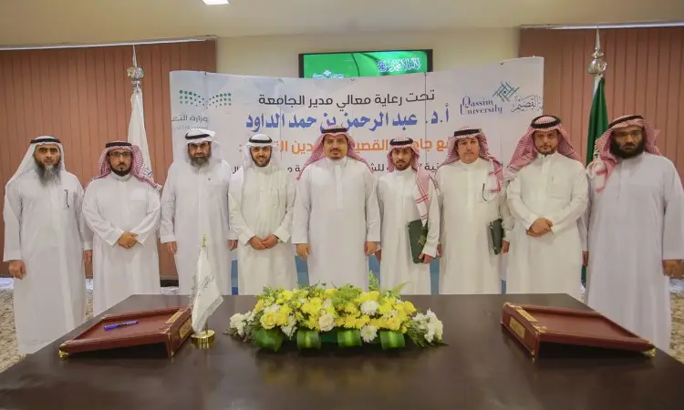 يجتمع عدد من الرجال مرتدين الزي السعودي الرسمي، بما في ذلك الشماغ أو الغترة السعودية، داخل القاعة أمام لوحة تحمل شعارات وأعلامًا للرجال. أكتب في صفحة متابعة الدراجة البخارية مستندات وزهورًا وتقريرًا يتعلق بالهدف الرابع عشر، وذلك ضمن إطار فعالية المجتمع في جامعة القصيم.