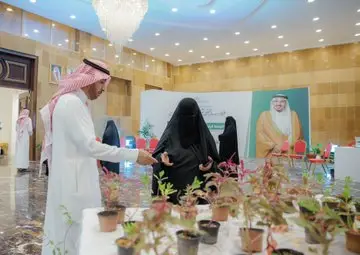 Men typically wear the Saudi shemagh and traditional dress, while women wear the black abaya and the niqab, in an exhibition held in Sitra al-Qa'iya. A discussion is held on what is related to the report on Goal 12, while small plants planted in the correct pots are distributed and a large picture hangs in the space.