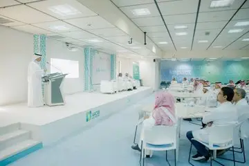 The man is usually a traditional Saudi in a podium inside a modern conference room, with a crowd of speakers, mostly clad in Saudi robes and shemagh, listening and taking notes. The discussions of the Goal 12 report will be projected on the screen with a number of viewers participating in the theater's panel discussion.
