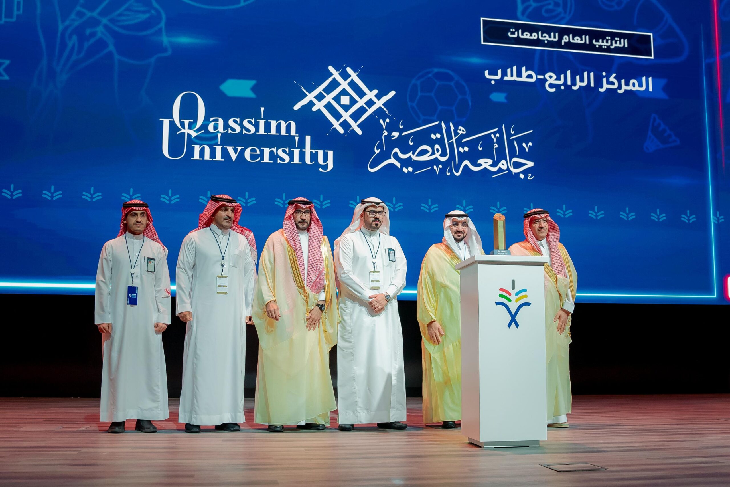 تكريم رسمي في جامعة القصيم جامعة القصيم بحضور ممثلين عن الجامعة وشاشة خلفية بشعار الجامعة.