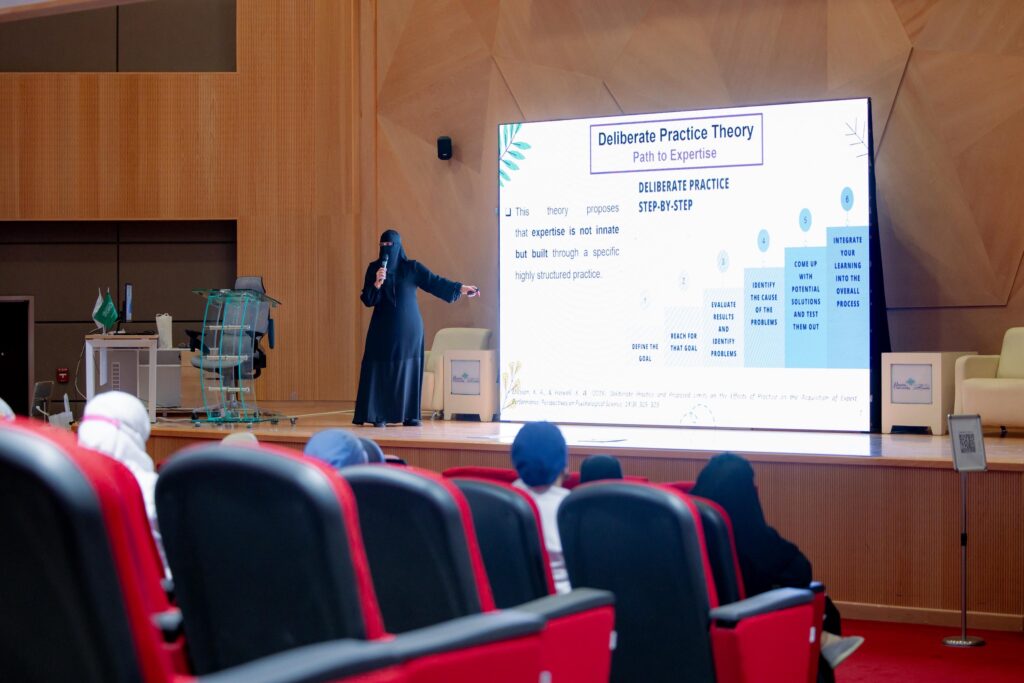 A faculty member gives an academic presentation on intentional training theory at a forum at Qassim University.