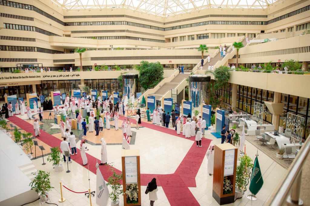 A modern hall hosts the simulation forum at Qassim University with identification pavilions and flags of the Kingdom.