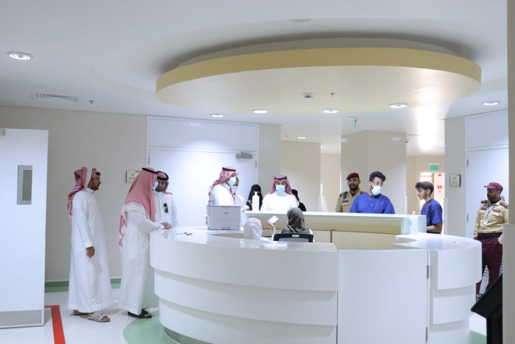 Discussing health awareness programs between Qassim University officials and hospital staff in a modern lobby.