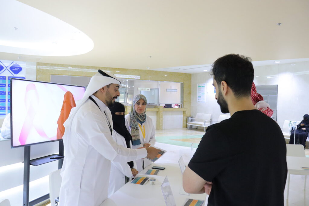 Awareness discussion about health programs at Qassim University with brochures distributed inside a modern academic hall.