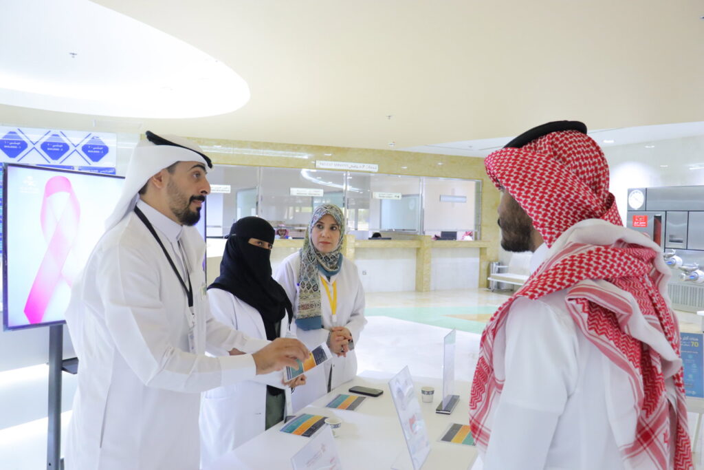 Discussing health awareness programs with a visitor at an academic event at Qassim University.