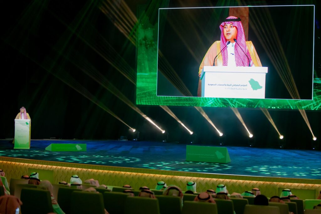 متحدث يلقي كلمة في مؤتمر جغرافي بجامعة القصيم بحضور أكاديمي في قاعة محاضرات.