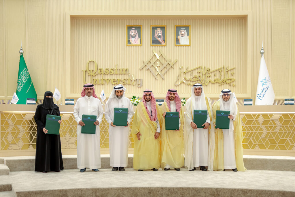 تكريم مشاركين مشاركين بجامعة القصيم وسط أعلام وصور وصور وطنية، في فعالية أكاديمية رسمية.