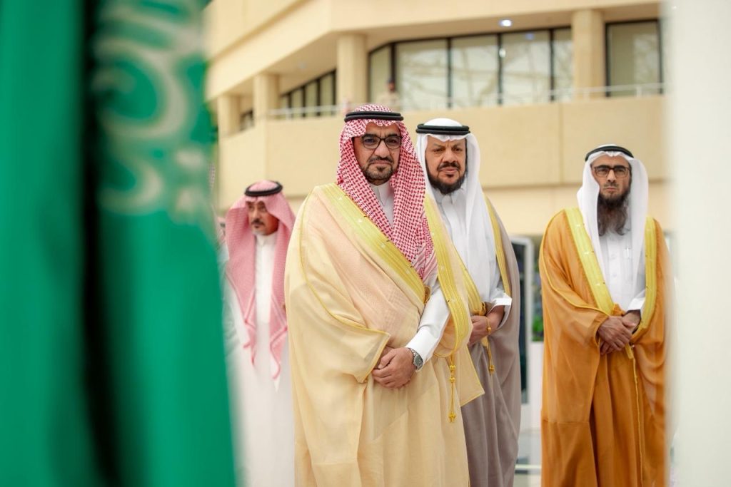 An official meeting at Qassim University with dignitaries and the Saudi flag in the foreground.
