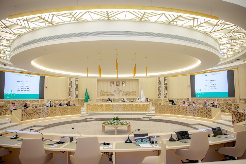 A formal meeting of the Deans of Student Affairs Committee at Qassim University in a modern, Saudi-themed hall.