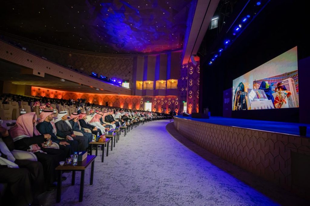 حضور أكاديمي رسمي في قاعة جامعة القصيم يتابع مؤتمرونًا علميًا وسط إنارة حديثة.
