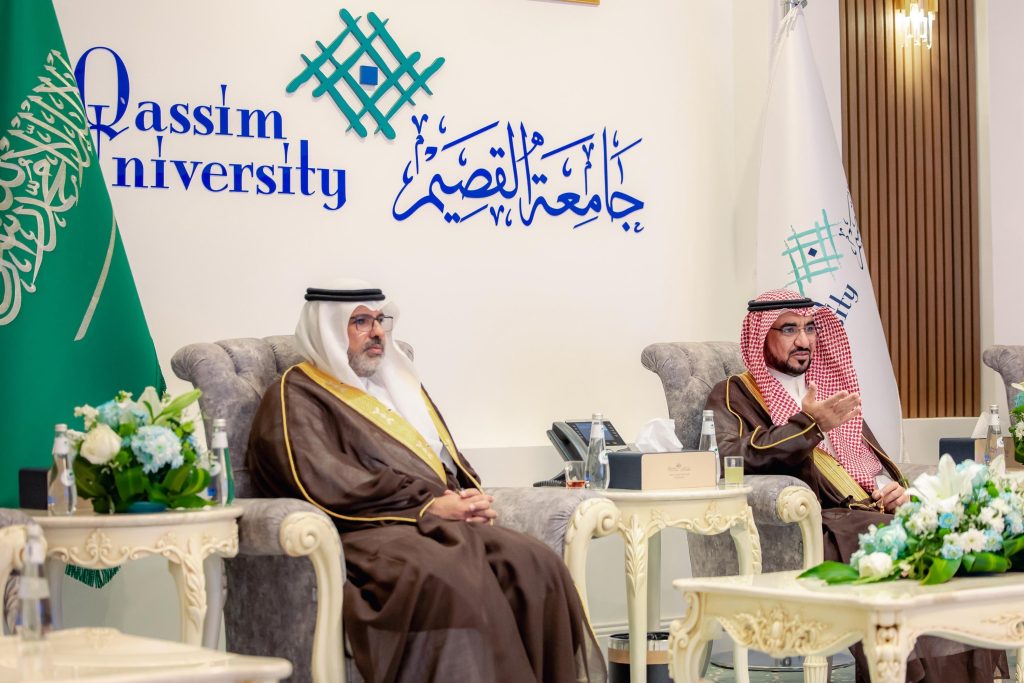 جلسة رسمية جامعة القصيم بحضور شخصيات سعودية، وشعار المدينة بارز في الخلفية.