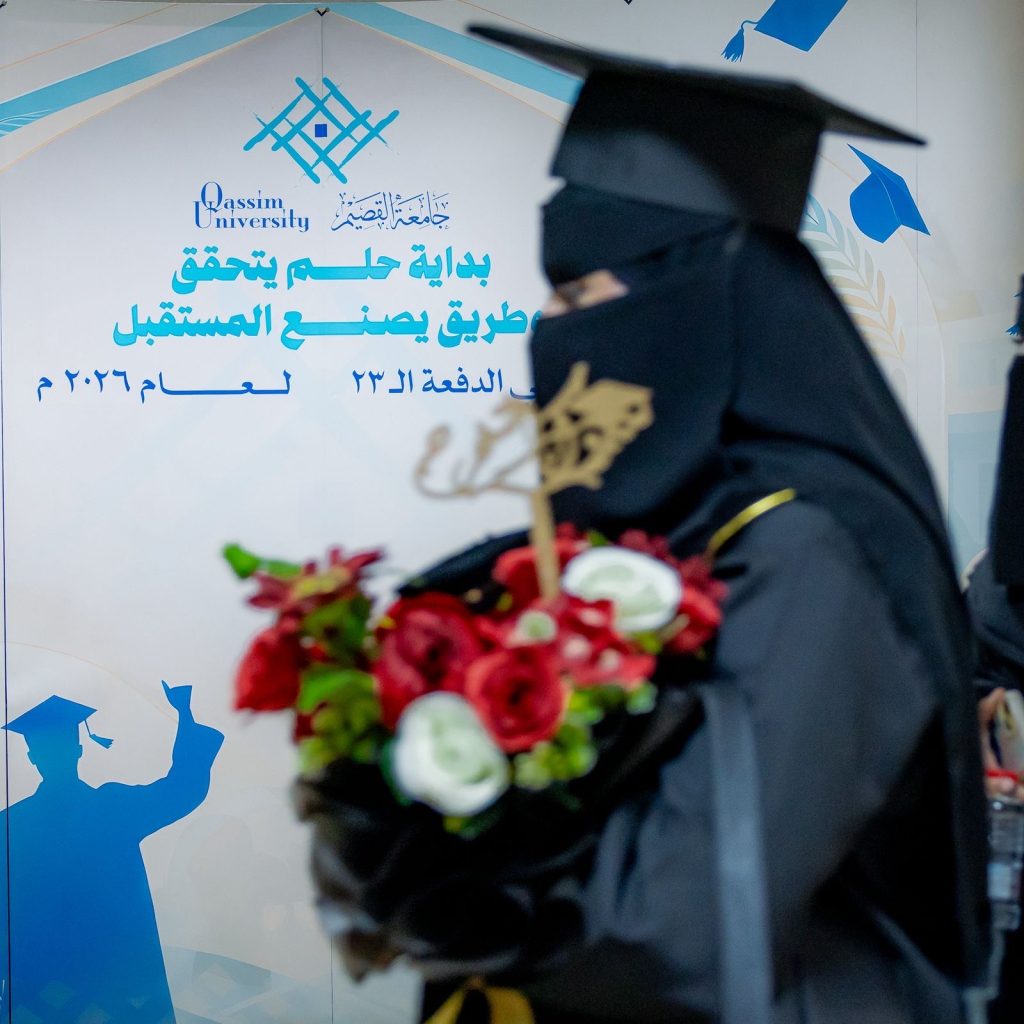 خريجة تحتفل بتخرجها أمام شعار جامعة القصيم في حفلات تخريج خريجي 2023-2024.