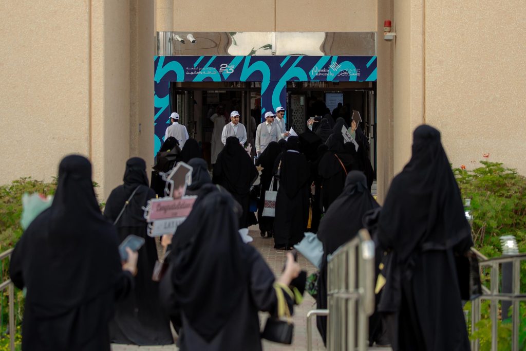 مشهد أكاديمي أمام مدخل جامعة القصيم يُوحي بحفل تخرج وحضور طلابي نشط.