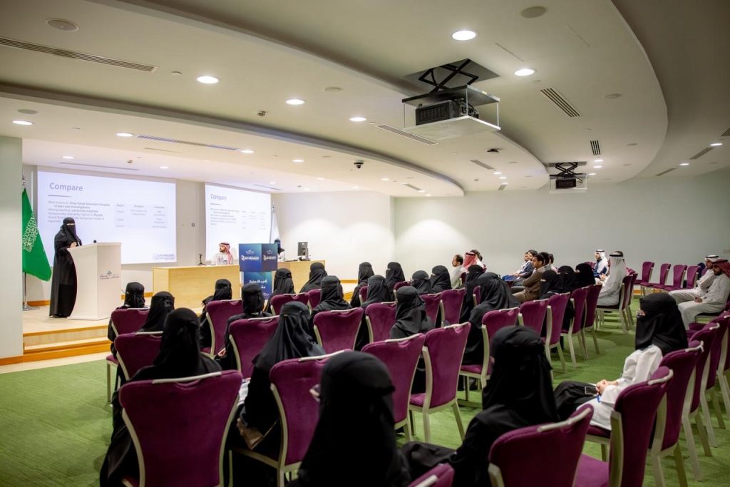 An academic lecture at Qassim University during the internship course, with the presence of a Saudi flag and a mariri show.