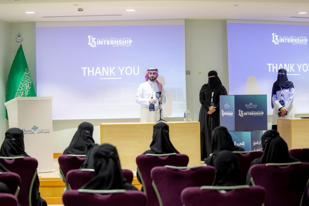 Giving a speech at the College of Medicine at Qassim University for the internship in the presence of the college staff, with the internship logo in the background.
