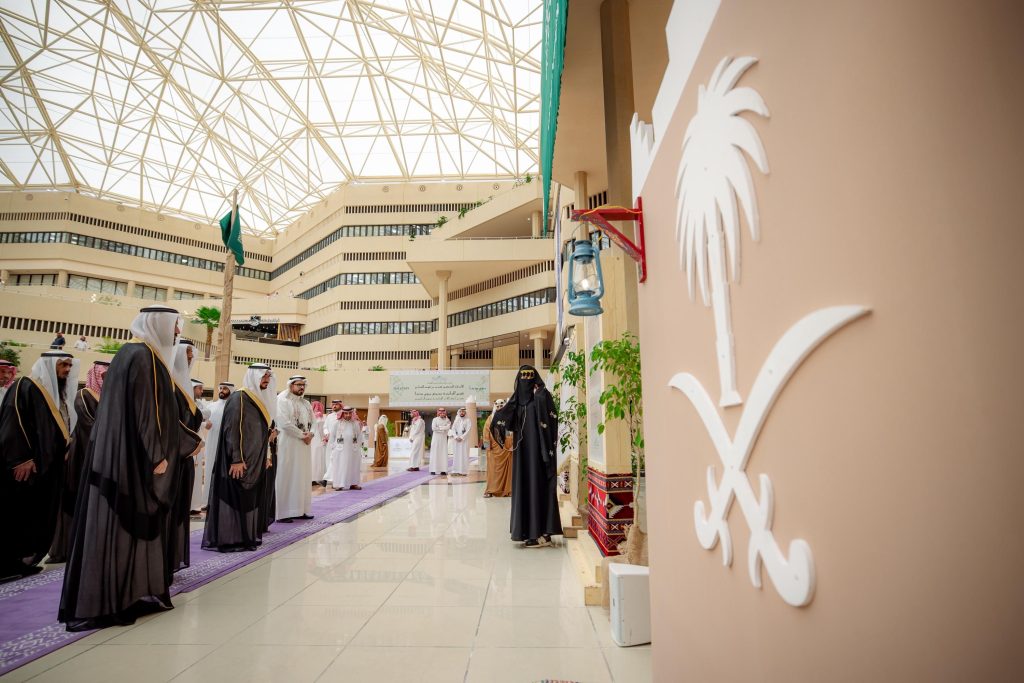 Qassim University President inaugurates the Badina Day Exhibition in the presence of university affiliates in a modern foyer.