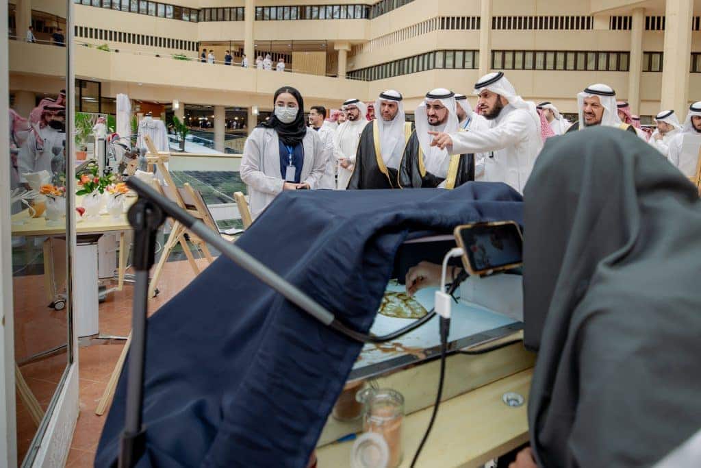 عرض علمي بجامعة القصيم حيث يشاهد الحضور تجربة الحضور مخبرية توثق بهواتفهم الذكية.