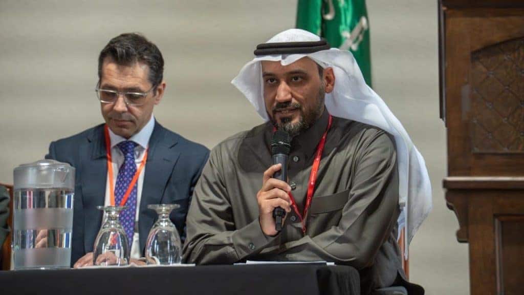 Qassim University participants discuss academic cooperation at the Educational Partnership Forum, in the presence of the Saudi flag.