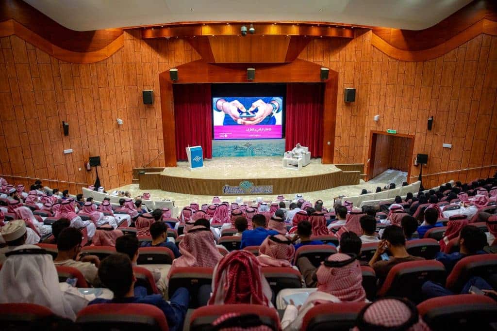 مؤتمر أكاديمي بجامعة القصيم بحضور جمع غفير، مع متحدثين وتقديمي على المسرح.