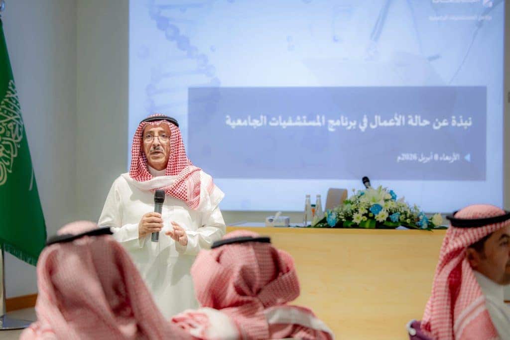 Al-Qassim member presents an academic presentation in front of attendees with the Saudi flag and Arabic text appearing.