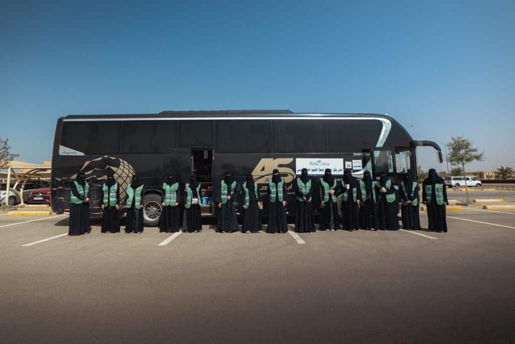 تنظيم أكاديمي لطالبات جامعة القصيم أمام حافلة جامعية في ساحة واضحة.