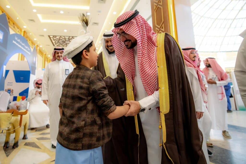 رئيس جامعة القصيم يكرم طفلاً خلال مهرجان مهرجان تراث الشعوب في فعالية أكاديمية.