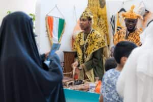 A cultural presentation at the Heritage Festival of Peoples at Qassim University, attended by university visitors and the flag of Ivory Coast.