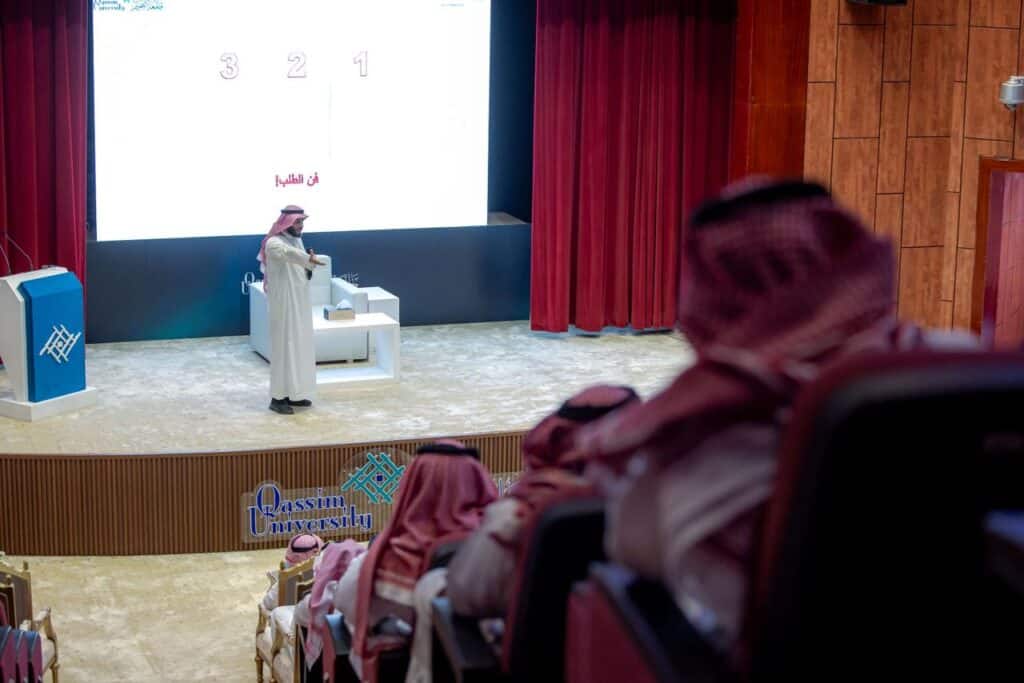 محاضر يقدم عرضًا عن التطوير المهني في قاعة محكمة القصيم مع شاشة تعرض محتوى علمي.
