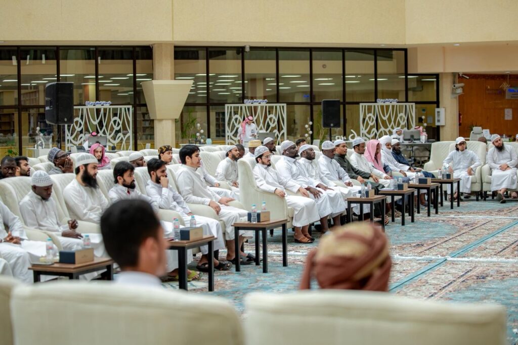 لقاء أكاديمي لطلبة جامعة القصيم في قاعة تتوسطها الطاولات والمكتبة بالخلفية.