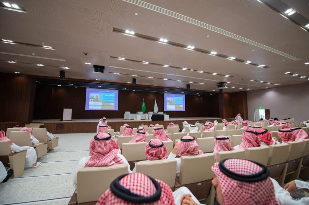 Leaders of Qassim University during official academic events in a hall decorated with the flags of the Kingdom of Saudi Arabia.