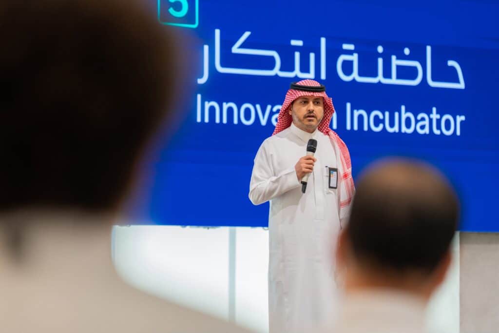 A speaker is presenting about the innovation incubator at an academic event at Qassim University.