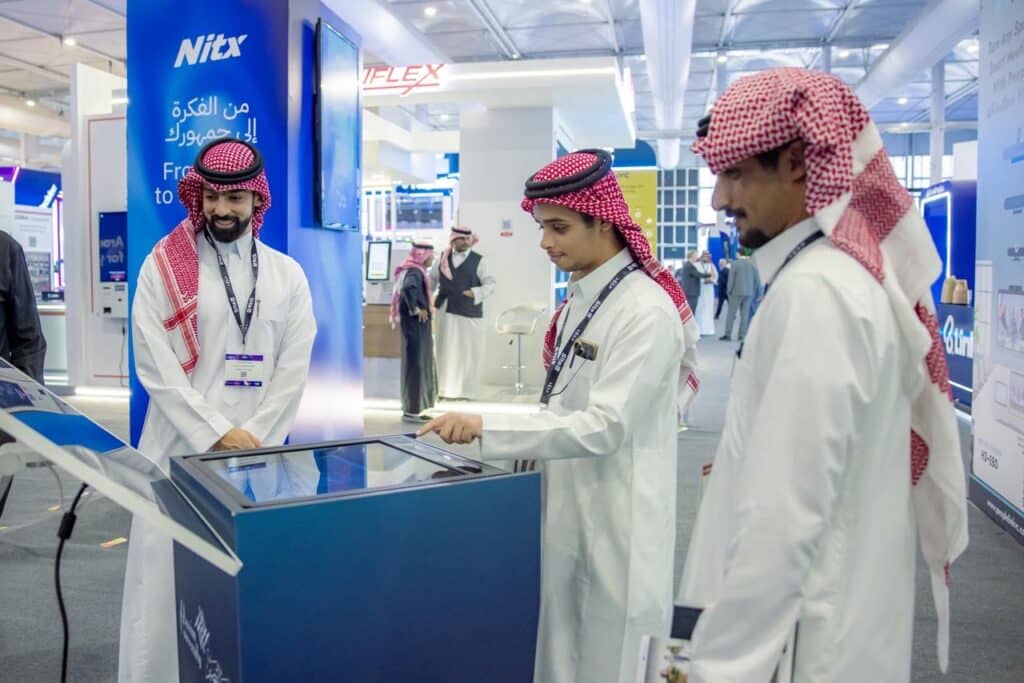 مشاركون من جامعة القصيم يتفاعلون مع عرض تكنولوجي في فعالية أكاديمية رسمية.