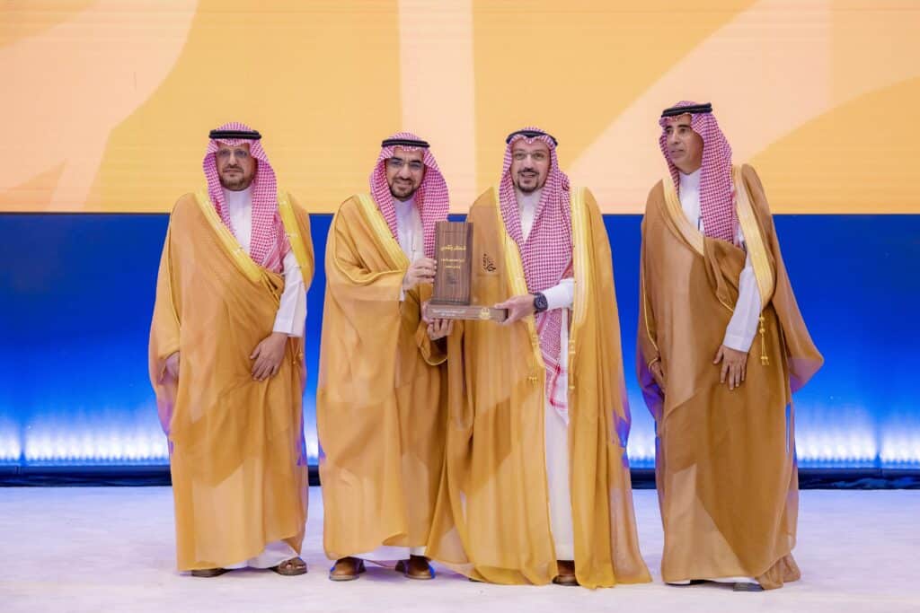تكريم أكاديمي لجامعة القصيم من خلال تبادل درع الإنجاز على خشبة المسرح.