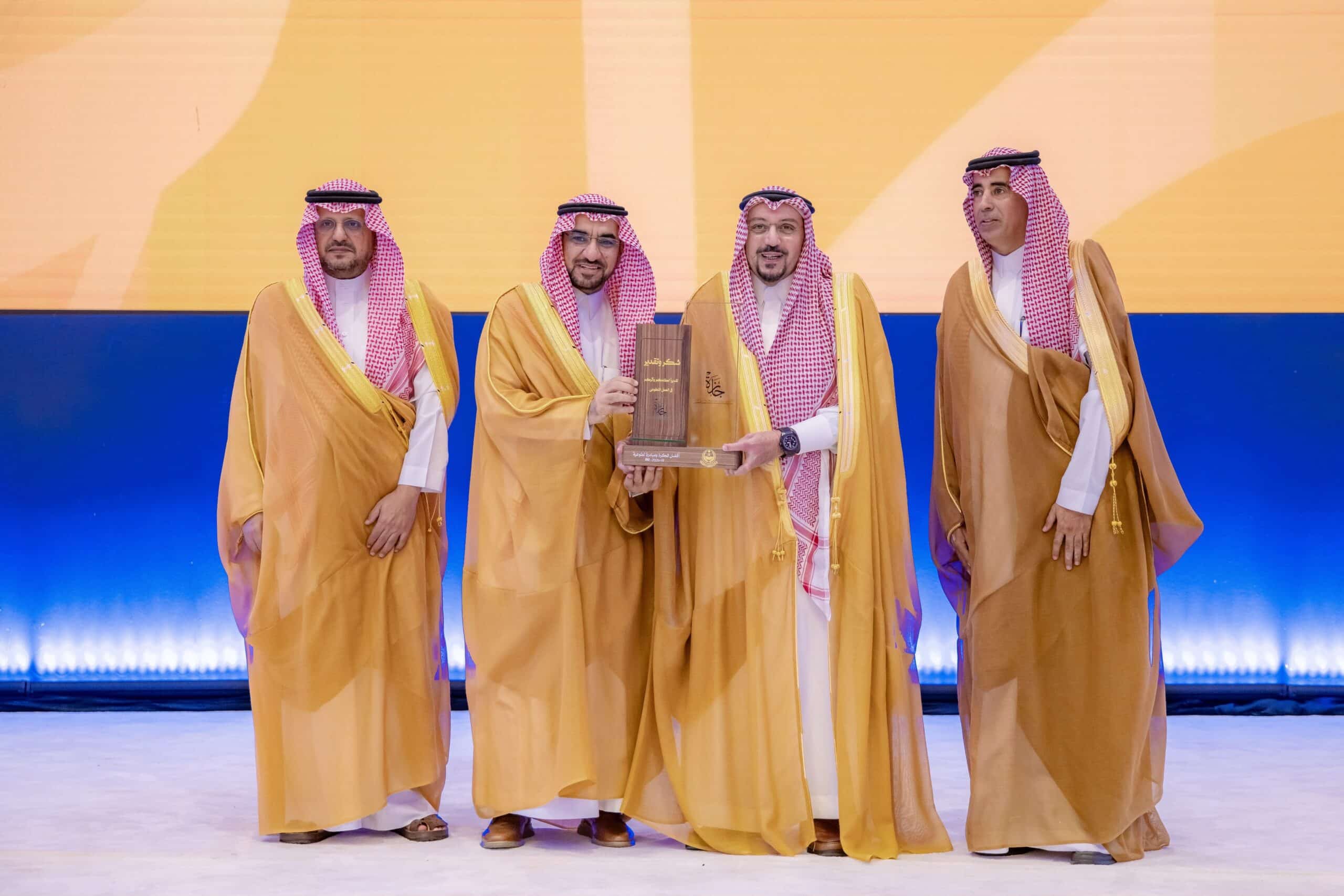 تكريم أكاديمي لجامعة القصيم من خلال تبادل درع الإنجاز على خشبة المسرح.