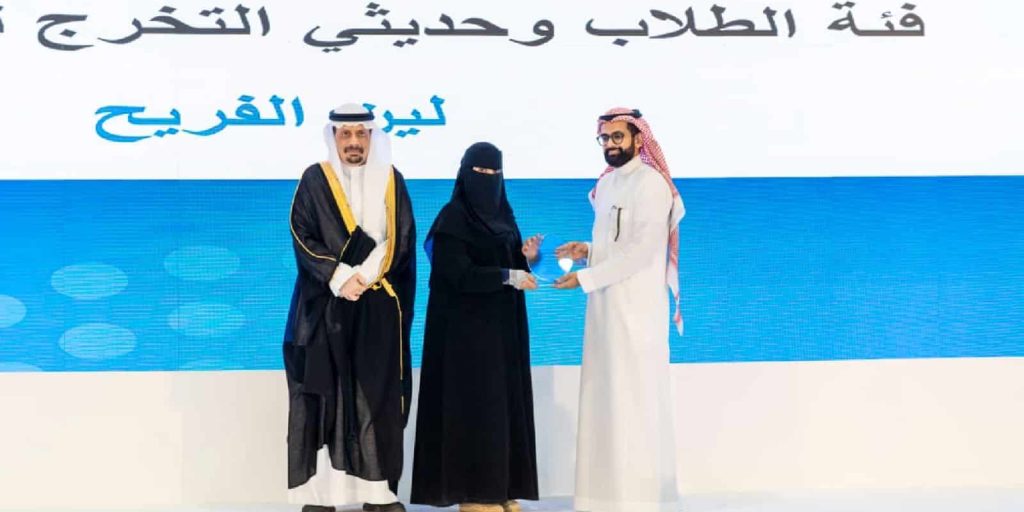 حفل تكريمي أكاديمي بجامعة القصيم تسليم جائزة بحضور شخصيات بارزة على المنصة.