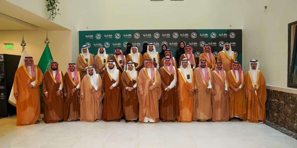 مسؤولون من جامعة القصيم في فعالية أكاديمية أمام شعار الجامعة والعلم السعودي.