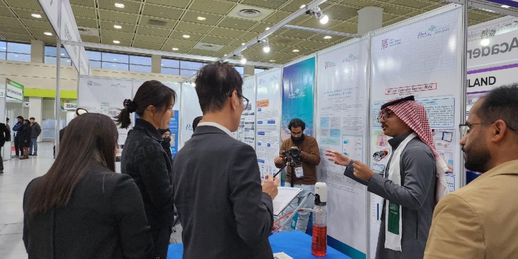 عرض مشروع علمي لطلاب جامعة القصيم في معرض أكاديمي، مع ملصقات وتجهيزات بحثية.