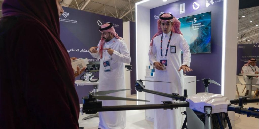 عرض تقني لطائرة دون طيار في جناح جامعة القصيم مع شاشات تعريفية ولافتات معلوماتية.